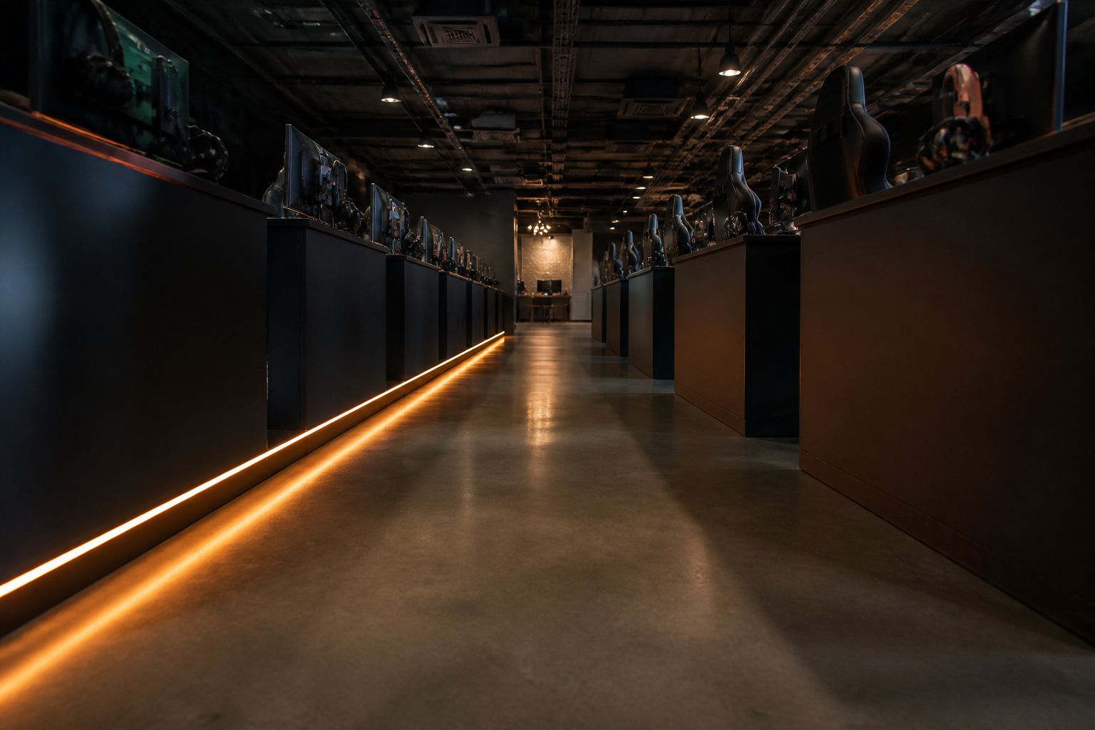 Low-angle view down a gaming lounge aisle with an orange light strip running along the desks